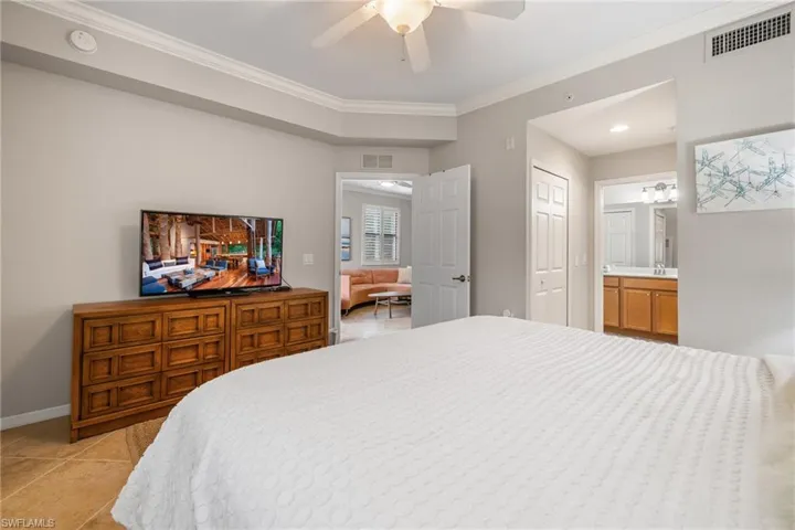 Bedroom with ensuite bath, sink, light tile patterned floors, ornamental molding, and ceiling fan