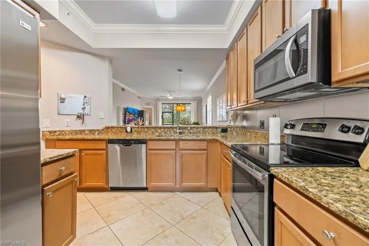 Kitchen with stainless steel appliances, light stone counters, kitchen peninsula, ornamental molding, and light tile patterned floors