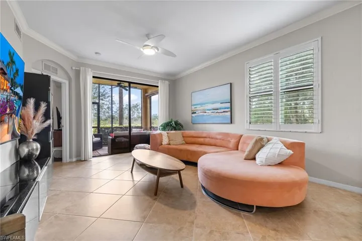 Living room with light tile patterned floors, ceiling fan, and crown molding