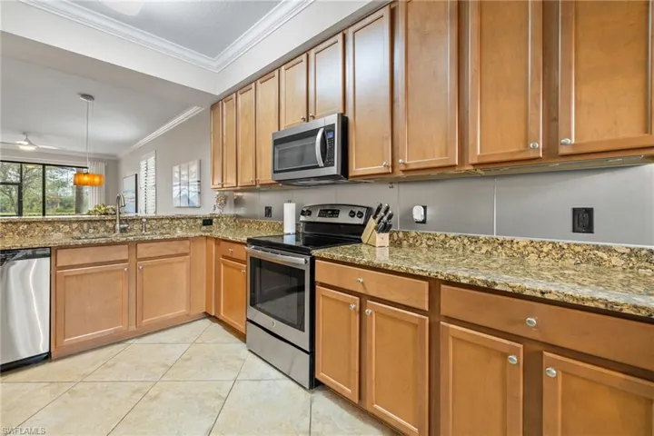 Kitchen featuring stainless steel appliances, light stone counters, sink, ornamental molding, and light tile patterned flooring