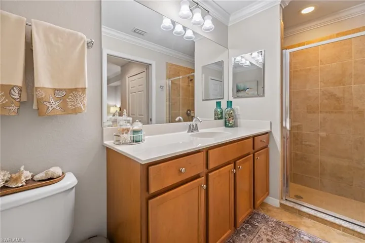 Bathroom with toilet, tile patterned floors, vanity, crown molding, and a shower with shower door