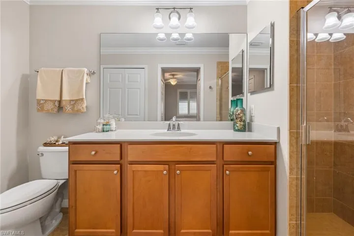 Bathroom featuring a shower with door, ornamental molding, ceiling fan, vanity, and toilet