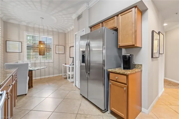 Kitchen featuring light tile patterned flooring, light stone counters, stainless steel fridge, and crown molding