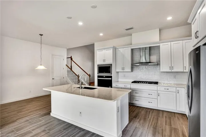 Kitchen with stainless steel kitchen appliances including wall oven, wall microwave, range hood, 36" gas cooktop, side-by-side refrigerator, and dishwasher