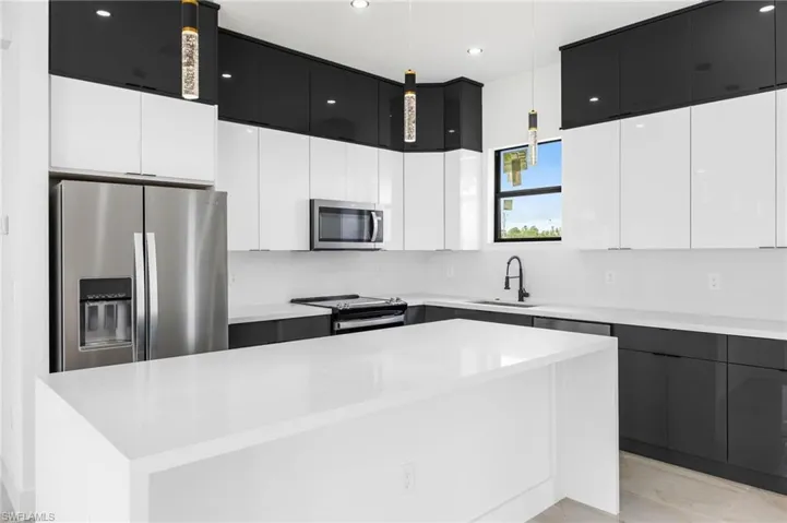Kitchen featuring stainless steel appliances, sink, decorative light fixtures, a center island, and white cabinetry