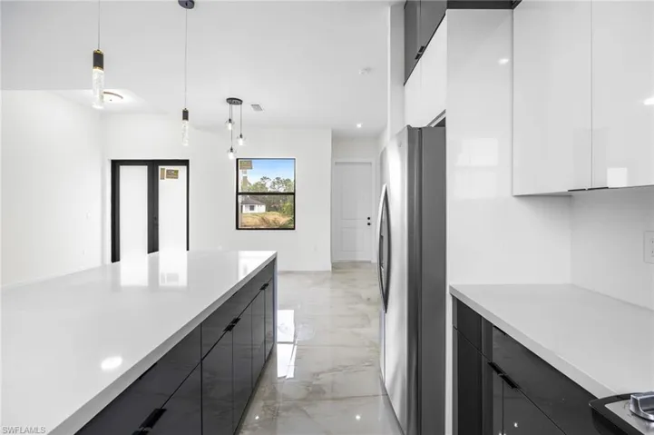 Kitchen with stainless steel refrigerator, white cabinetry, and decorative light fixtures