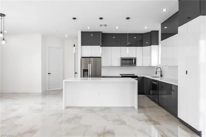 Kitchen with sink, a kitchen island, pendant lighting, white cabinets, and appliances with stainless steel finishes