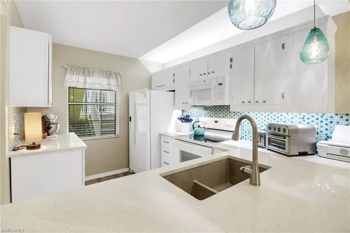 Kitchen with pendant lighting, tasteful backsplash, white appliances, and white cabinetry