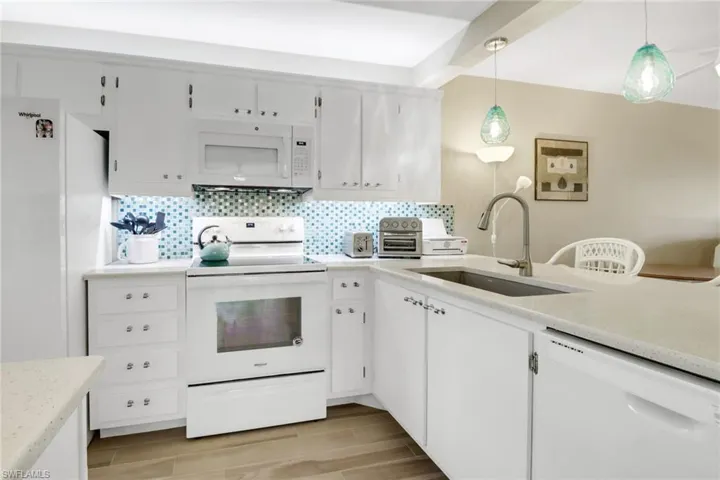 Kitchen with white cabinets, white appliances, decorative light fixtures, and sink