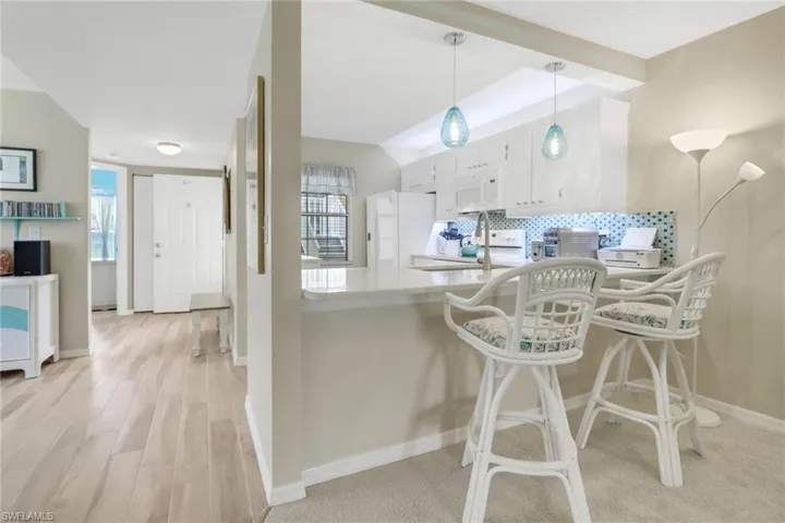 Kitchen with white cabinets, tasteful backsplash, white appliances, light hardwood / wood-style flooring, and decorative light fixtures