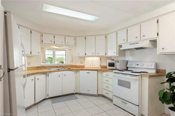 Kitchen with white appliances, white cabinets, light tile patterned floors, and wooden counters