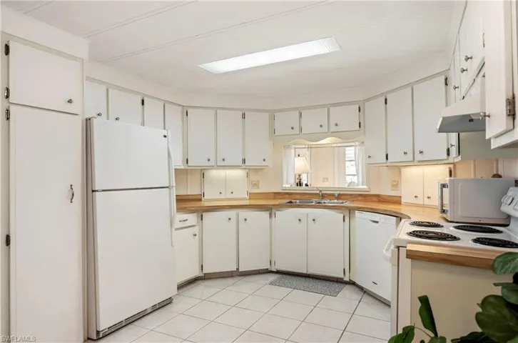 Kitchen featuring white appliances, light countertops, white cabinets, and light tile patterned floors