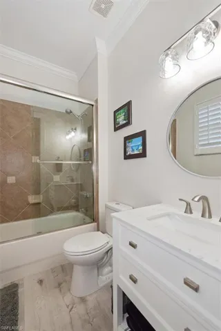 Full bath with vanity, enclosed tub / shower combo, light wood finished floors, and ornamental molding