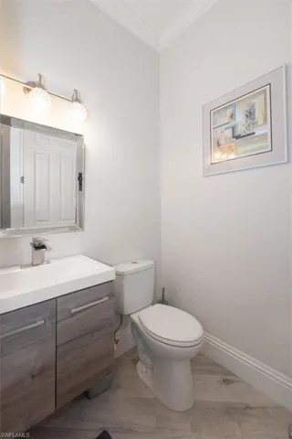 Half bath with vanity, ornamental molding, and light wood finished floors