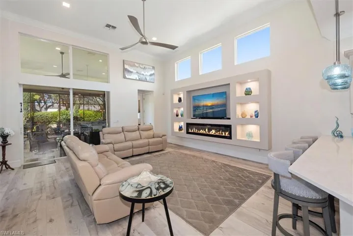 Living area with ornamental molding, a high ceiling, light wood-style flooring, a glass covered fireplace, and recessed lighting
