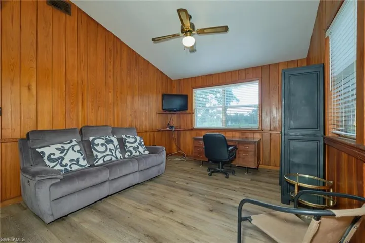 Office space with ceiling fan, vaulted ceiling, wood walls, and light hardwood / wood-style floors