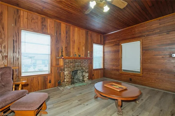 Living room with ceiling fan, dark hardwood / wood-style flooring, wooden walls, wooden ceiling, and a fireplace