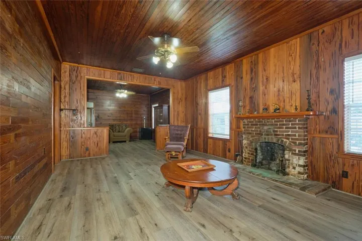 Sitting room with ceiling fan, wood ceiling, wood walls, a brick fireplace, and hardwood / wood-style floors