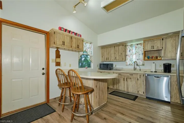 Kitchen featuring stainless steel dishwasher, a breakfast bar, vaulted ceiling, light hardwood / wood-style floors, and kitchen peninsula