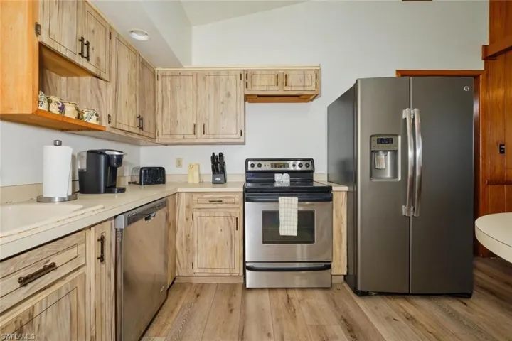 Kitchen with stainless steel appliances, light hardwood / wood-style flooring, light brown cabinetry, and lofted ceiling