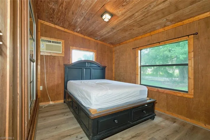 Bedroom featuring hardwood / wood-style flooring, wooden walls, a wall mounted AC, and multiple windows