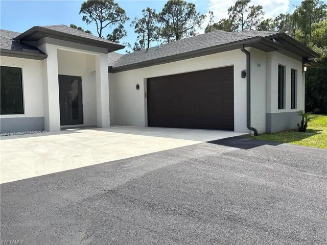View of front facade with stucco siding, roof with shingles, driveway, and a garage