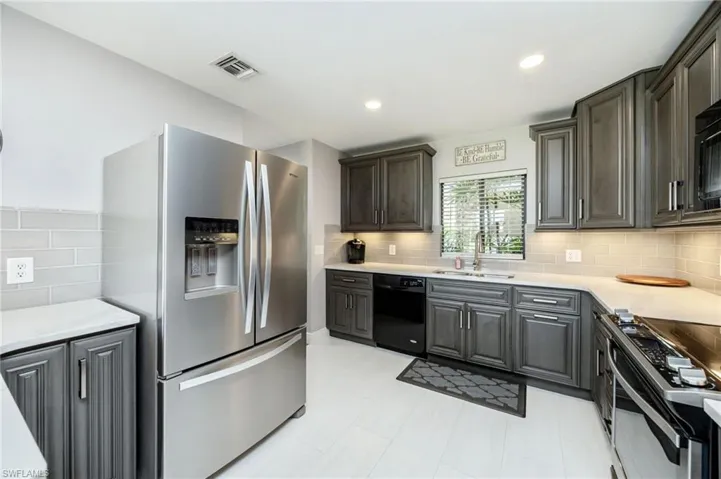 Kitchen with black appliances, light stone counters, recessed lighting, decorative backsplash, and gray cabinets