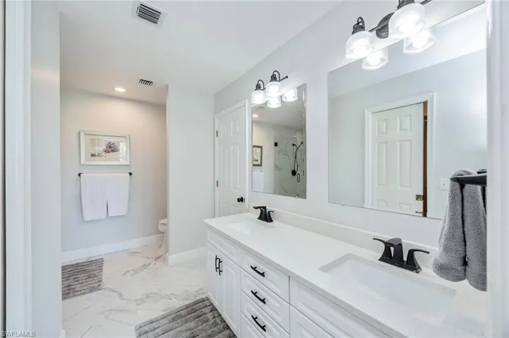 Full bathroom featuring a marble finish shower, double vanity, light marble finish floors, and recessed lighting