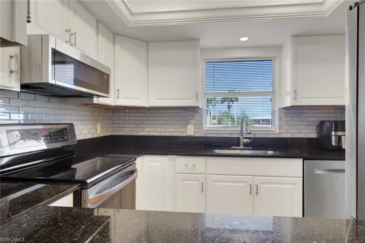 Updated kitchen with stainless steel appliances, white cabinetry, dark stone countertops, and light wood-style flooring