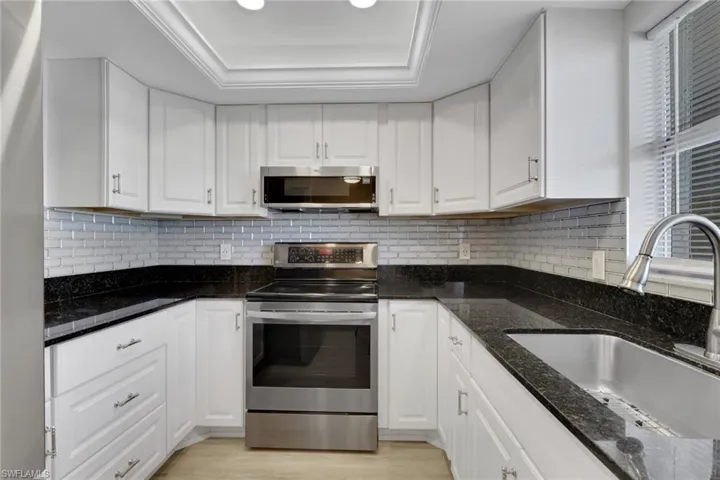 Updated kitchen with stainless steel appliances, white cabinetry, dark stone countertops, and light wood-style flooring