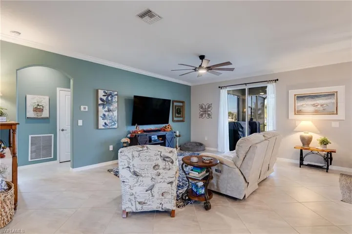 Living room with crown molding, arched walkways, light tile patterned floors, and a ceiling fan