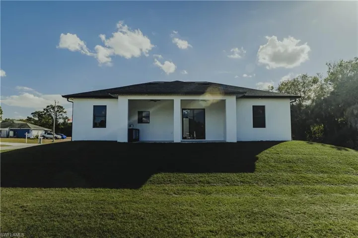 Rear view of house featuring a lawn, stucco siding, and yard area.