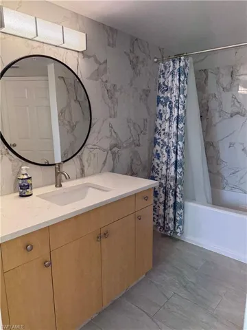 Full bath with tile walls, shower / tub combo, vanity, and light marble finish floors