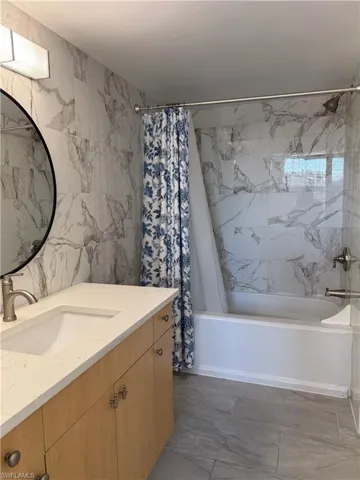 Full bathroom with vanity, shower / bath combo with shower curtain, and tile walls