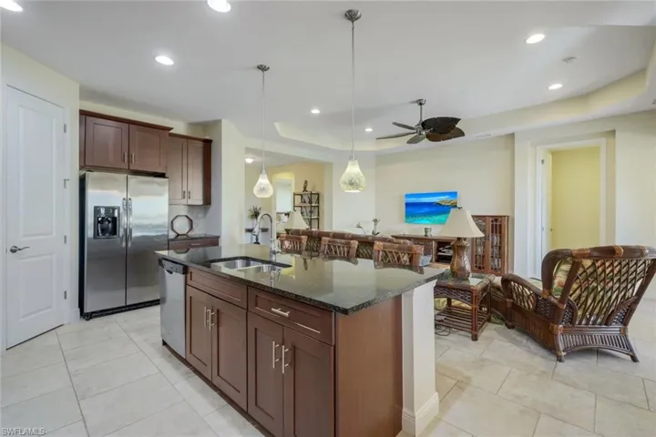 Kitchen with dark stone counters, appliances with stainless steel finishes, a tray ceiling, hanging light fixtures, and dark brown cabinets