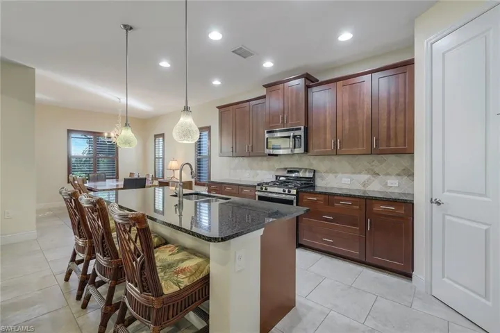 Kitchen with dark stone counters, decorative backsplash, stainless steel appliances, a breakfast bar area, and decorative light fixtures