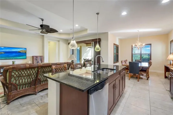 Kitchen with dark stone countertops, stainless steel dishwasher, decorative light fixtures, a kitchen island with sink, and a chandelier