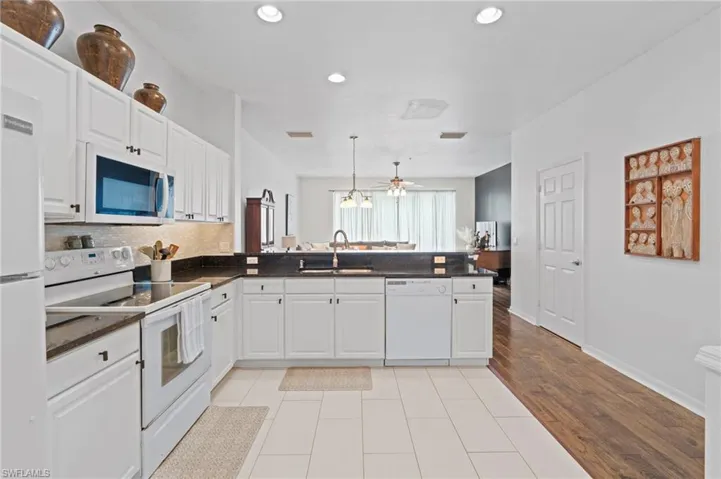 Kitchen featuring white appliances, white cabinets, a peninsula, and a ceiling fan