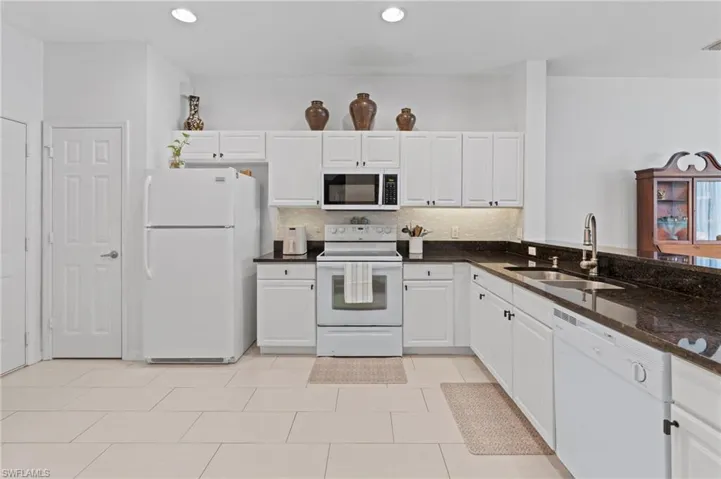 Kitchen with white appliances, white cabinets, dark stone counters, decorative backsplash, and light tile patterned floors