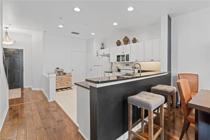 Kitchen with light wood-type flooring, white appliances, white cabinetry, a peninsula, and decorative backsplash