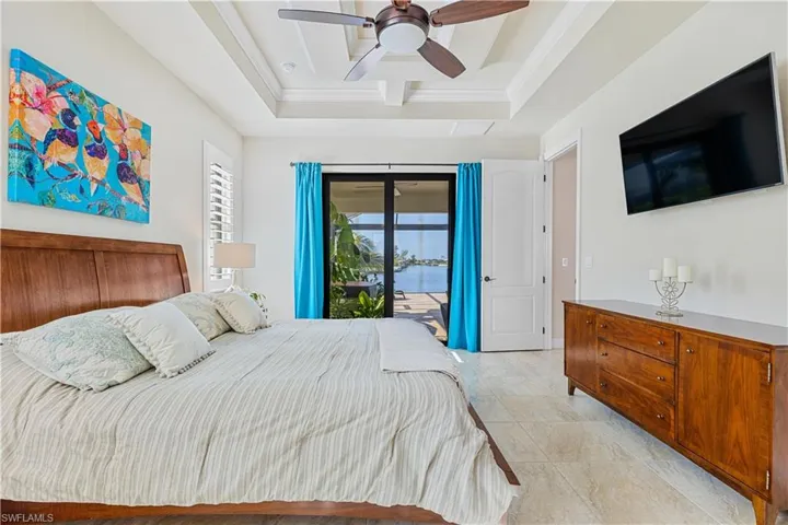 Tiled bedroom with ceiling fan, access to exterior, and a tray ceiling