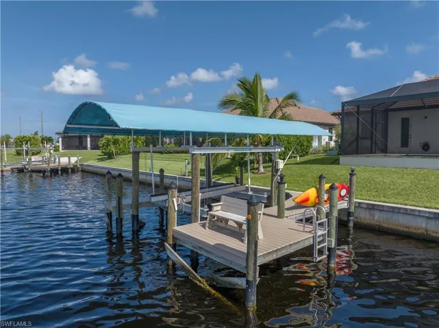 View of dock with a lanai, a water view, and a lawn