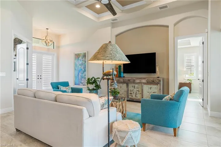 Living room with light tile patterned flooring, a wealth of natural light, coffered ceiling, and ceiling fan with notable chandelier