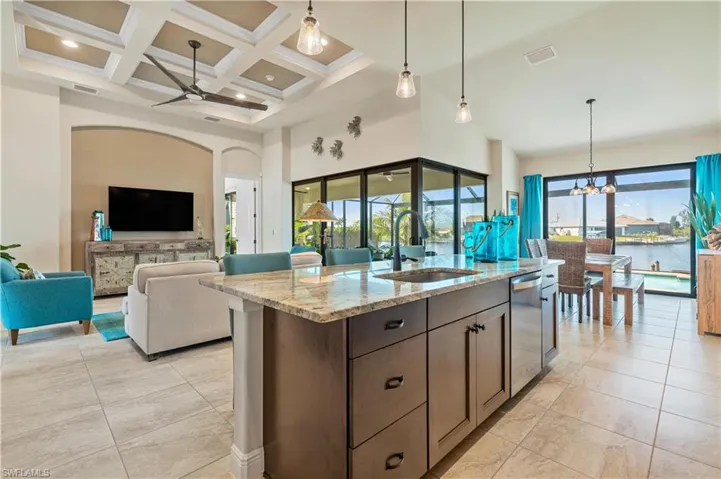 Kitchen featuring stainless steel dishwasher, light stone countertops, coffered ceiling, decorative light fixtures, and sink