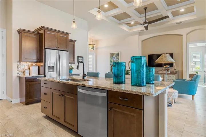 Kitchen with ceiling fan, beamed ceiling, coffered ceiling, appliances with stainless steel finishes, and a kitchen island with sink
