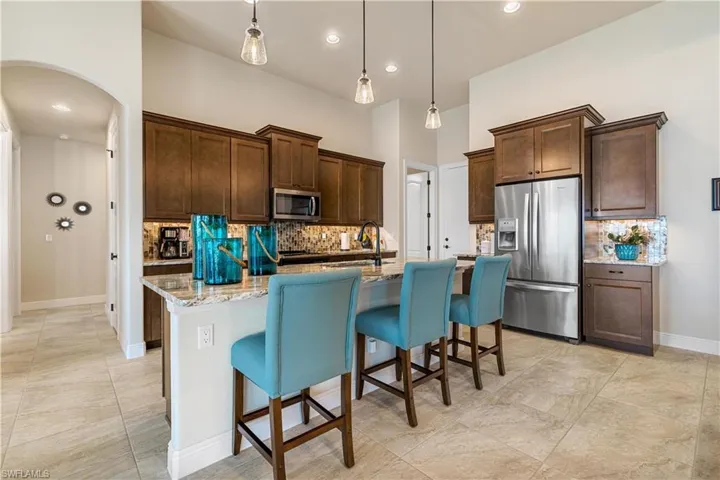 Kitchen with a center island with sink, appliances with stainless steel finishes, tasteful backsplash, and light stone counters