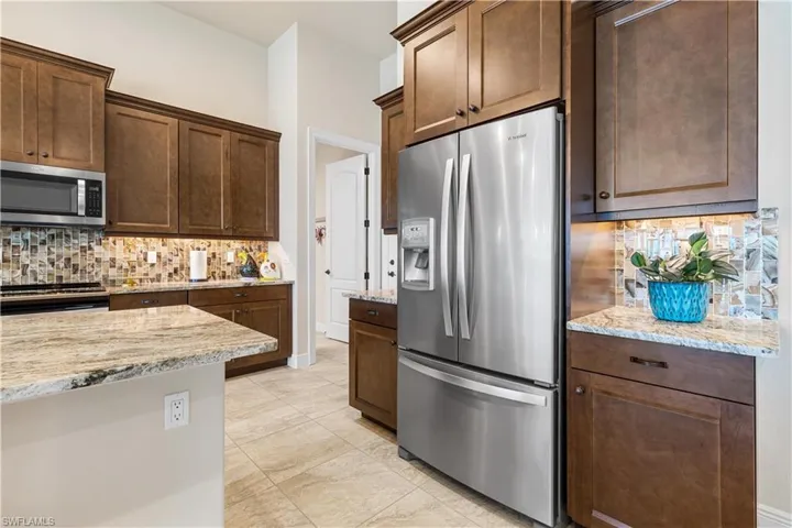 Kitchen featuring light tile patterned flooring, light stone counters, stainless steel appliances, and backsplash