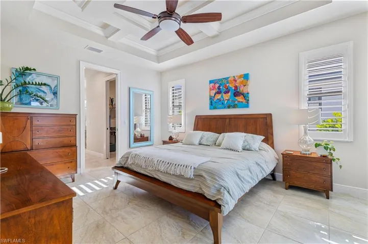 Tiled bedroom featuring a tray ceiling, crown molding, coffered ceiling, and ceiling fan