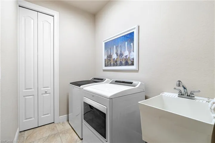 Laundry room with light tile patterned floors, washer and clothes dryer, and sink