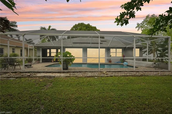 Back house at dusk featuring a patio, a lawn, and a lanai